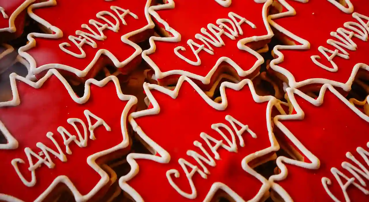 Red maple leaf cookies with white icing outline and “CANADA” written on top.