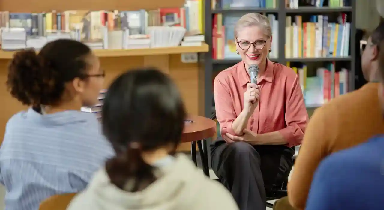 A smiling woman with glasses speaks into a microphone during a small group discussion.