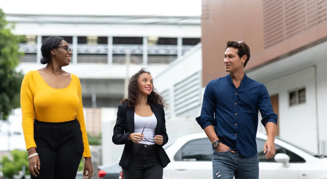 Tres personas sonrientes caminan juntas al aire libre, conversando de manera casual.