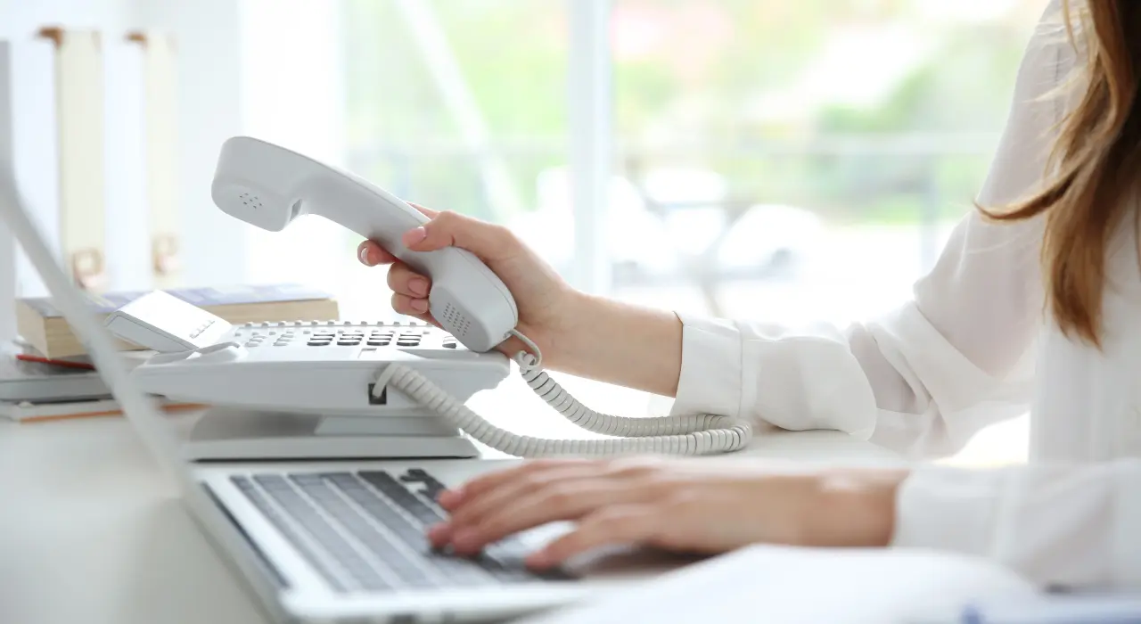 ਇੱਕ ਵਿਅਕਤੀ ਟੈਲੀਫ਼ੋਨ ਦਾ ਰਿਸੀਵਰ ਫੜ੍ਹ ਕੇ ਲੈਪਟਾਪ ‘ਤੇ ਟਾਈਪ ਕਰ ਰਿਹਾ ਹੈ।