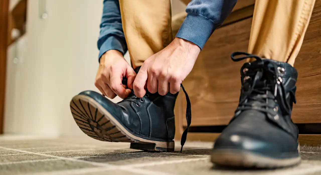 Primer plano de una persona atándose los cordones de unas resistentes botas negras, preparándose para salir.