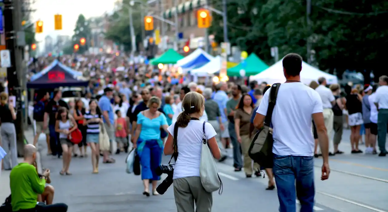 A large crowd of people attending a lively outdoor street festival lined with tents and booths.