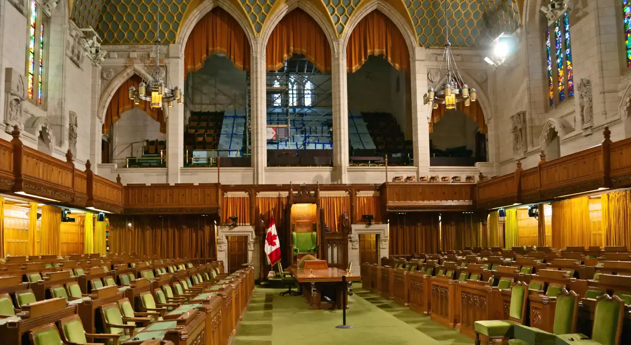 ਓਟਾਵਾ ਦੀ ਹਾਊਸ ਆਫ ਕਾਮਨਜ਼ ਦੇ ਅੰਦਰ ਦਾ ਦ੍ਰਿਸ਼, ਹਰੇ ਸੀਟਾਂ, ਲੱਕੜ ਦੇ ਪੈਨਲ ਅਤੇ ਕੈਨੇਡੀਅਨ ਝੰਡੇ।