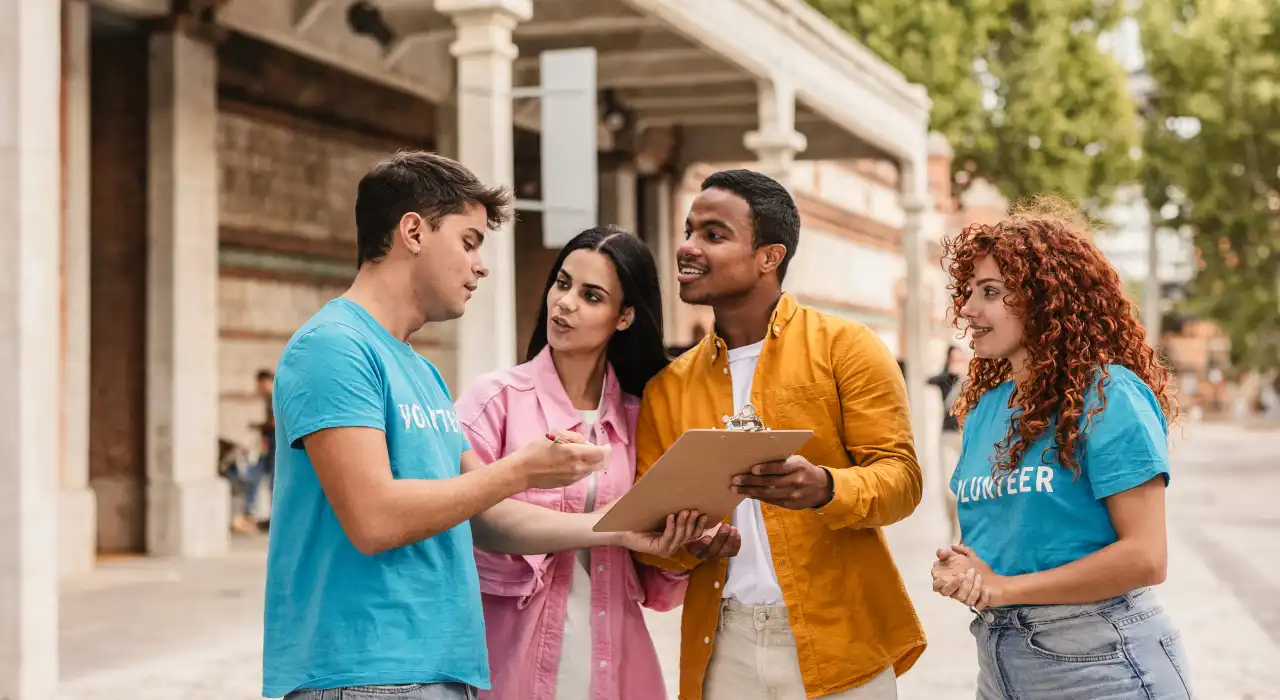 Four volunteers talking outdoors, with one holding a clipboard while others listen and engage in discussion.
