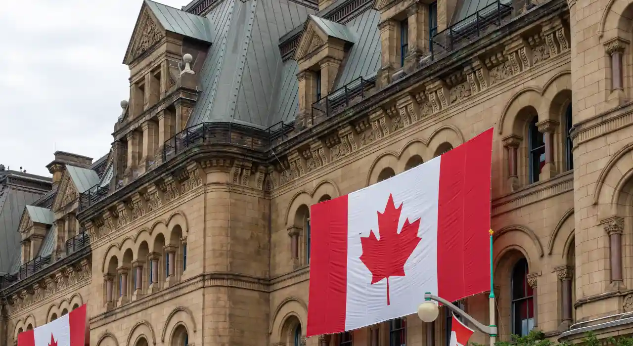 Large Canadian flag hanging on the exterior of a historic government building in Ottawa.