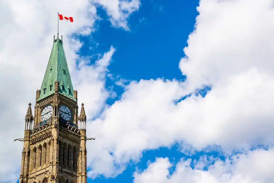 Parliament Hill clock tower in Ottawa with Canada flag against blue sky.